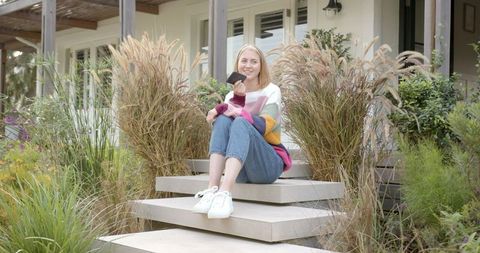 Woman Relaxing Outdoors with Smartphone Near Modern Home