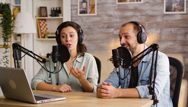 Two hosts recording casual conversation podcast in cozy home studio with headphones