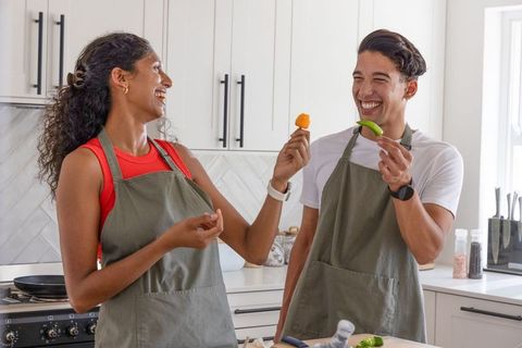 Couple laughing while taste-testing peppers at bright modern kitchen island