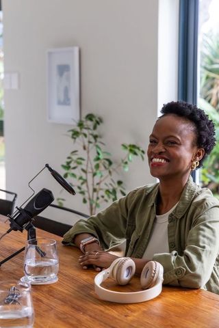 African american woman smiling and speaking into condenser microphone during podcast recording