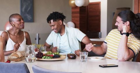 Multiracial friends laughing and sharing appetizers around modern dining table at home