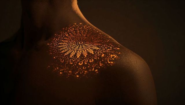 Amber mandala glowing on shoulder with moisture droplets in dark studio