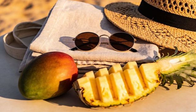 Sunlit tropical picnic with sliced pineapple, mango, straw hat, round sunglasses