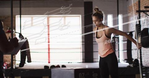 Preparing woman doing plyo box jump near boxing ring with coach holding clipboard