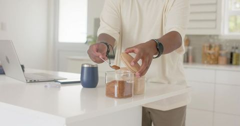African american man scooping brown sugar from jar on modern white kitchen island