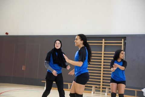 Teen volleyball team practicing in school gym wearing blue-black jerseys and knee pads