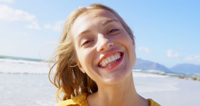A young Caucasian woman smiles brightly at the camera, with copy space. Her joyful expression and the beach setting convey a sense of happiness and relaxation.