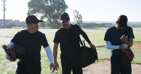 Diverse baseball teammates walking across dew-covered infield at dawn carrying gear