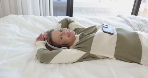 Woman Relaxing on Bed Listening to Music with Wireless Headphones