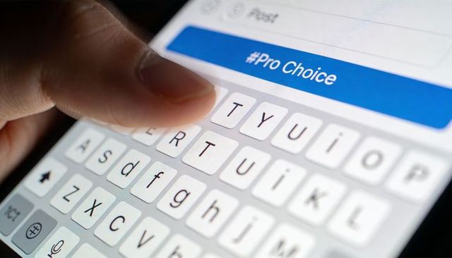 Tapping Finger on Smartphone Keyboard Displaying #ProChoice Hashtag in Low Light