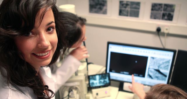 Happy caucasian female student with others using microscope and computer in medical lab - Download Free Stock Photos Pikwizard.com