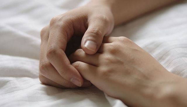 Clasped hands conveying comfort and connection on soft striped linen bed, morning light