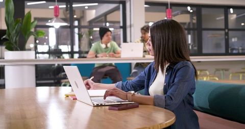 African American woman working on laptop in modern coworking space with colleagues