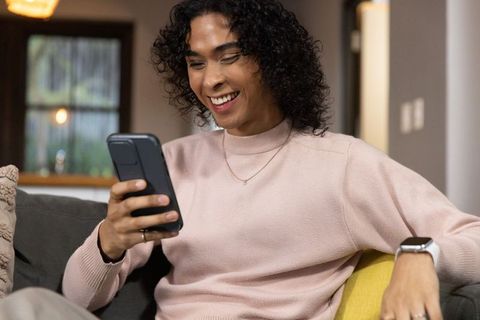 Smiling non-binary person relaxing on couch using smartphone and smartwatch