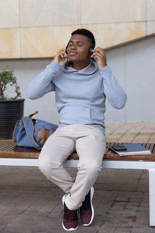 African american teen student sitting on bench listening to music with headphones