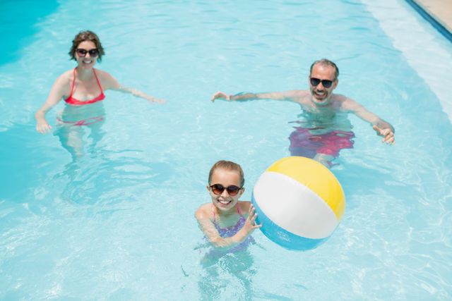 Family enjoying a sunny day in a swimming pool, playing with a beach ball. Perfect for advertisements related to summer vacations, family activities, outdoor fun, and leisure time. Can be used in travel brochures, family-oriented product promotions, and lifestyle blogs.