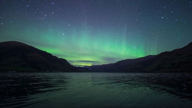 Aurora borealis dancing over mountain lake reflecting green bands under starry sky