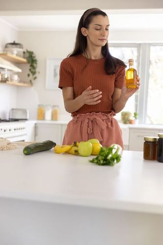 Woman inspecting olive oil bottle while preparing fresh produce on kitchen island