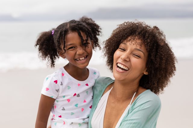 Portrait of happy African American Mother and daughter standing together at beach on a sunny day