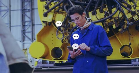 Technician tapping tablet in industrial workshop with yellow machinery and safety gear