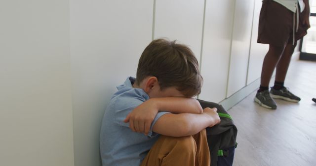 Image of sad caucasian boy sitting at school corridor, covering head with hands. primary school education, knowledge and learning concept.