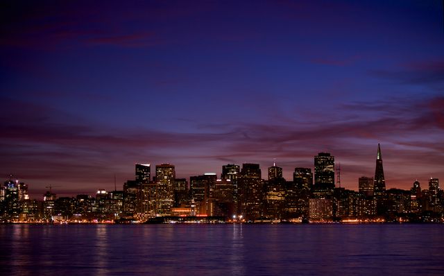 San Francisco skyline at twilight with illuminated city lights reflecting on calm water. Perfect for travel promotions, city lifestyle advertisements, blog headers about urban living, or promotional material for local businesses.