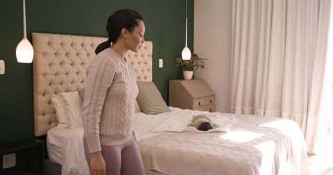 Mother watching swaddled infant in cozy bedroom under double lamps