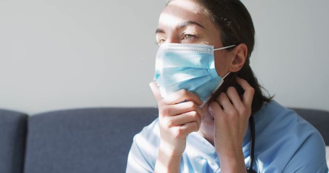 Caucasian female doctor wearing face mask at home sitting on couch. medicine, health and healthcare services during coronavirus covid 19 pandemic.