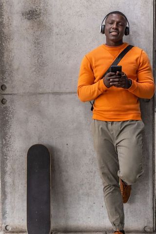 Leaning against concrete wall listening to music while checking smartphone