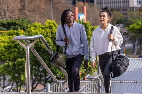 Diverse friends walking up urban stairs carrying gym duffel bags wearing hoodies
