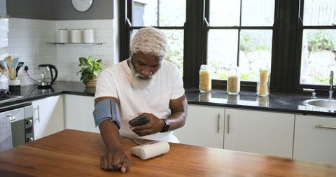 Senior man using digital blood pressure monitor at kitchen island