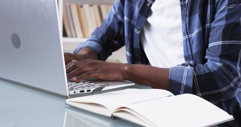 Man Working on Laptop While Notetaking in Home Workspace