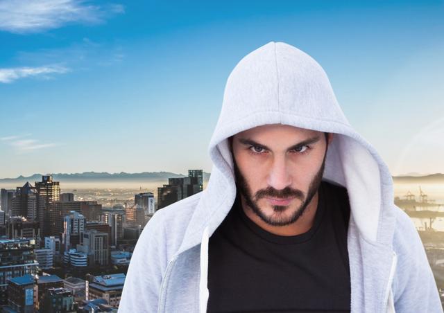 Depicts a man with a serious expression wearing a gray hooded sweatshirt. In the background, a bustling cityscape with modern buildings and a clear blue sky enhances the urban atmosphere. This image can be used to represent themes like urban life, determination, street style, or modern youth culture. Suitable for advertisements, blogs, social media posts focusing on fashion, lifestyle, urban living, or personal motivation.