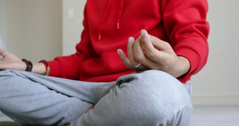 Man meditating cross-legged at home wearing red hoodie and gray sweatpants