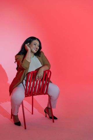 Confident plus-size asian woman on red chair smiling in studio with crimson backdrop