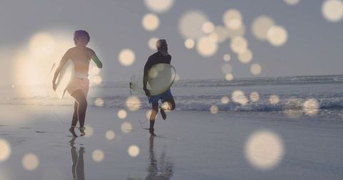 Running pair carrying surfboards along sunrise shoreline with bokeh light reflections