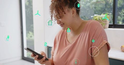Woman using smartphone in kitchen managing home energy app with eco icons