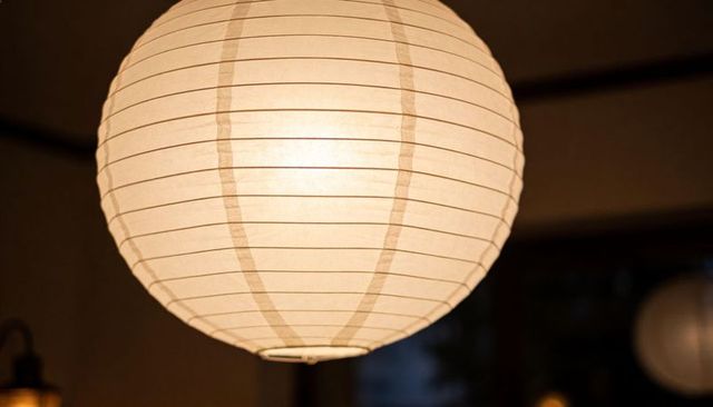 Glowing round paper lantern hanging in cozy interior, warm ambient globe lighting design