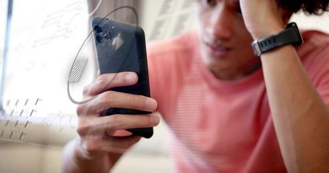 Young man studying smartphone with financial graphs and wearable fitness watch in casual home