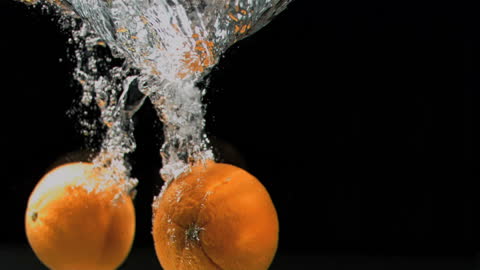 Two Fresh Oranges Splashing in Water Against Black Background