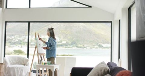 Senior woman painting by waterfront window in bright minimalist studio