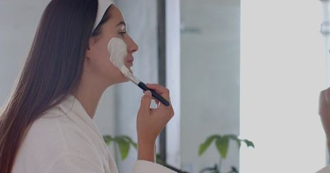 Relaxed Young Woman Applying Skincare Mask by Bathroom Mirror
