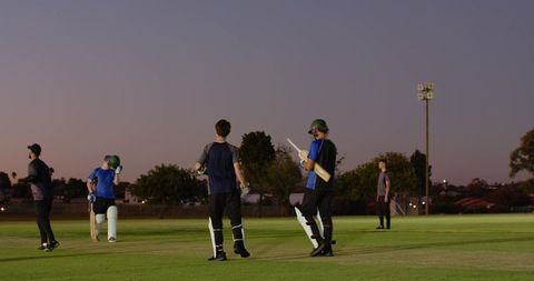 Teenage cricketers crossing mid-pitch at dusk under floodlights practicing batting partnership