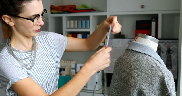 Young Caucasian woman tailors a garment on a mannequin at home. Her focus on crafting bespoke clothing illustrates a passion for fashion design.