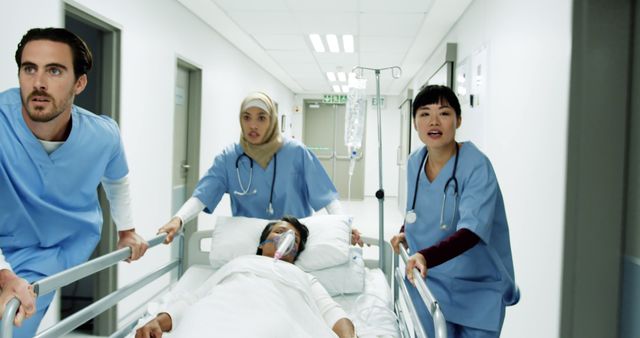 Medical team urgently transporting patient on stretcher through hospital corridor. Keywords can support content for healthcare, emergency services, teamwork in medical facilities, or diversity in medical professions.