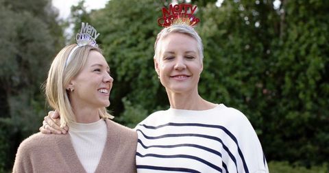 Senior and middle-aged friends smiling while wearing merry christmas headbands in garden