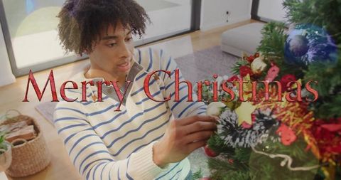 Young man decorating christmas tree in cozy living room in striped sweater placing ornament