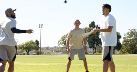 Diverse male teammates batting and fielding during outdoor cricket practice on sunny day