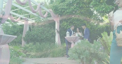 Smiling bride flanked by men in suits under draped pastel pergola at garden reception