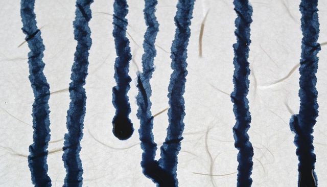 Blue ink bleeding through fibrous paper with vertical streaks and droplet texture